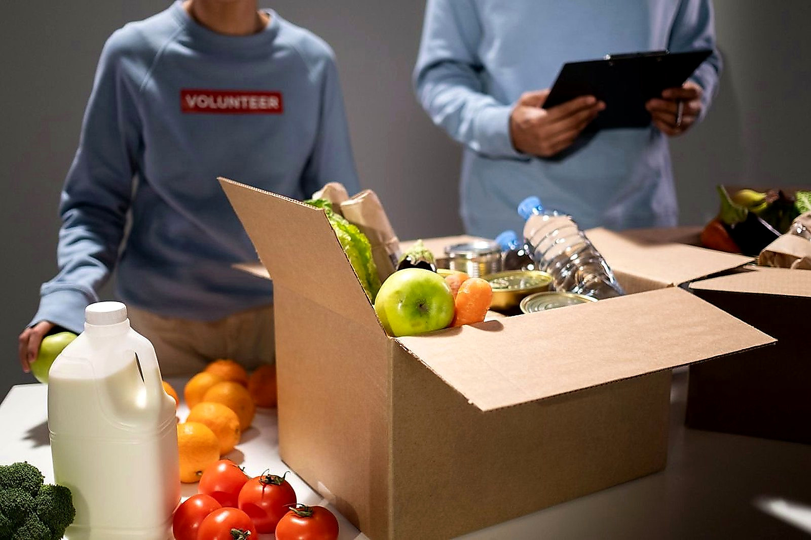 Free People packing a cardboard box with essentials like fruits, vegetables, and bottled water for charity. Stock Photo