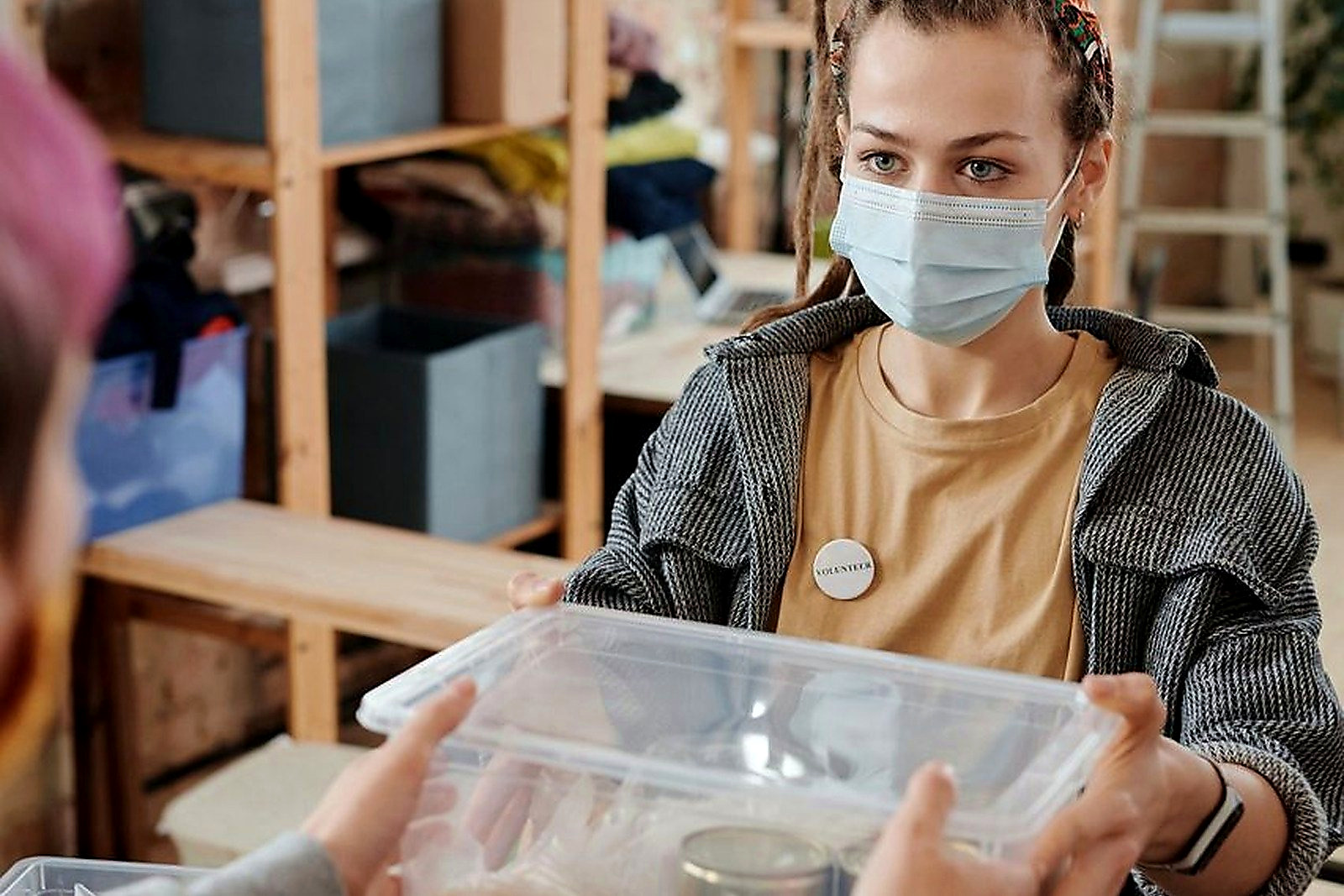 Free A young woman in a mask hands a food donation box in an indoor facility. Stock Photo